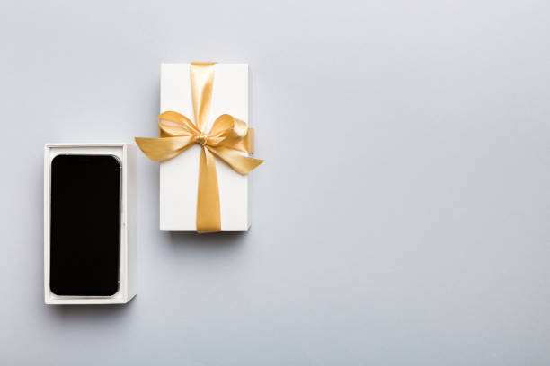 istock Opened gift box with gold ribbon and smartphone on color background, top view. Blank open box packaging mockup , Template for your design - branding mockup 1753775592