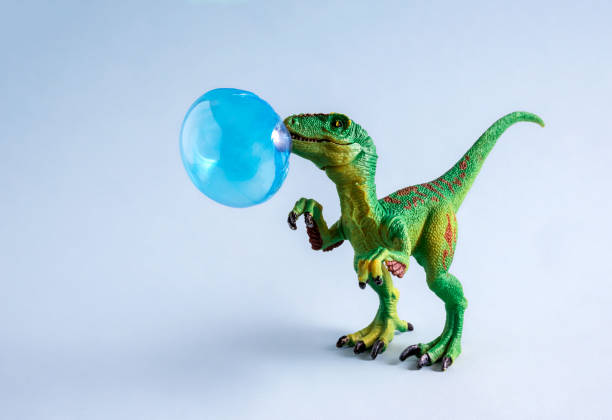Happy green toy dinosaur with blue chewing gum bubble on blue background.