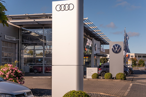 Neuwied, Germany -October 21, 2023:  a pylon with the AUDI logo in front of another one with  the VW logo (Volkswagen) and the showroom of the local AUDI and VW car dealer