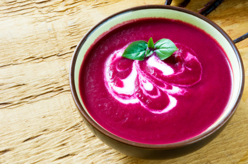 A bowl of beet soup with a swirl of yogurt, basil and black pepper.