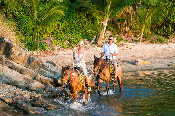 Couple horseback ridding on rocky beach