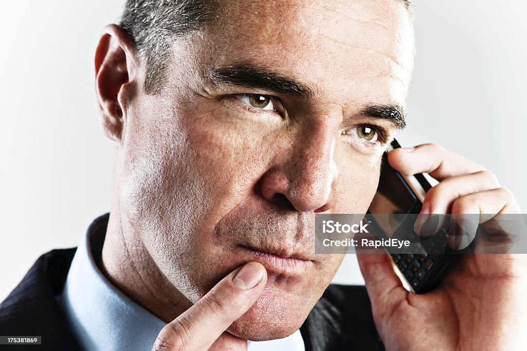 Handsome businessman on cellphone considers something seriously "Close-up shot of a handsome and serious businessman with his mobile phone, finger to his lips as he considers either what he's hearing or what to say next." 30-39 Years Stock Photo