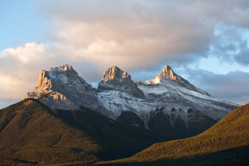 The Three Sisters mountains in Canmore, Alberta, Canada. This beautiful mountain massif is one of the most famous in the Canadian Rockies. The mountains are located just south of the Canmore townsite and are visible from most places in the charming mountain town. In this image they are sidelit on a late fall sunset. Nobody is in the image, taken with Canon 5D Mark II camera body. Landscape image of iconic Alberta scene. 