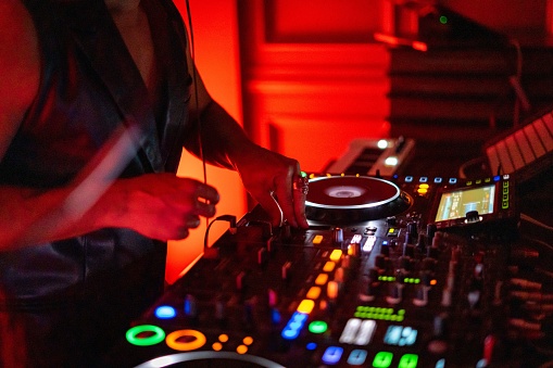 A DJ working on a professional controller in a dimly lit room, with illuminated buttons