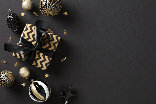 Christmas frame. Luxury Xmas gift box with gold and black decorations on dark background. Christmas banner mockup, festive cover template. Flat lay, top view, copy space.