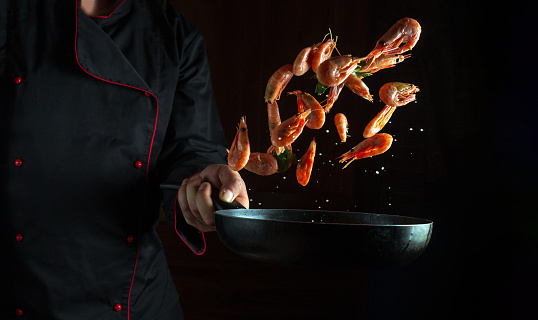 Cooking shrimp in a frying pan in the hand of a chef. Diet concept with seafood on black background