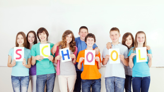 Cheerful preteen students standing in front of the whiteboard and showing colorful  SCHOOL message on white placards.
