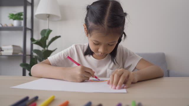 Cute Asian girl painting color on a paper enjoys with color at home. Kid home schooling