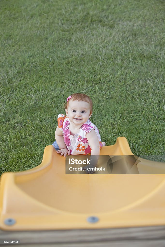 Baby Girl at Bottom of Yellow Slide Baby girl looking up and smiling from the bottom of a slide. 6-11 Months Stock Photo