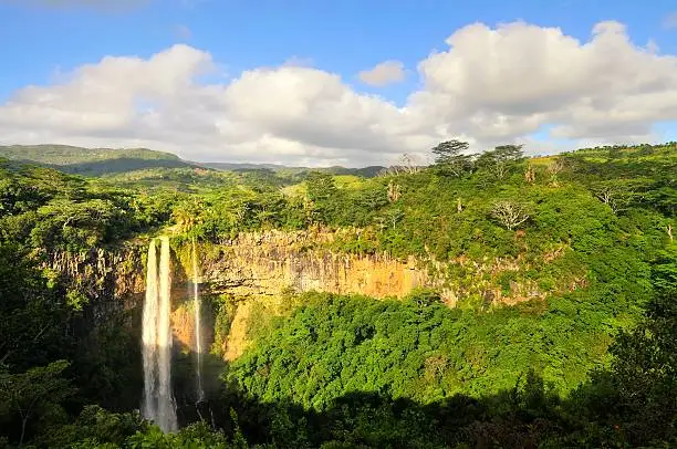 The Chamarel waterfall in Mauritius in late afternoon with the sun cutting across the gorge and the seemingly infinite fields beyind