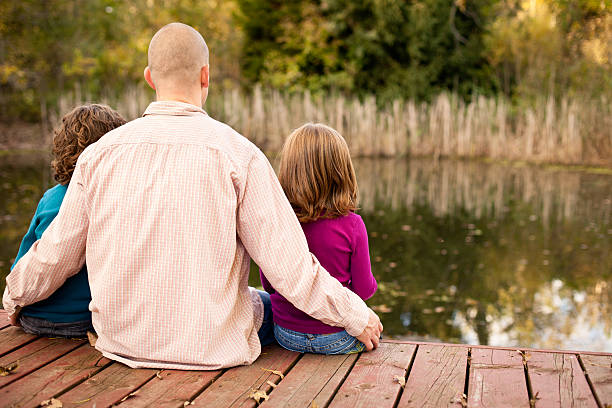 istock Dad Sitting Outside By Water With His Little Daughters 175384240