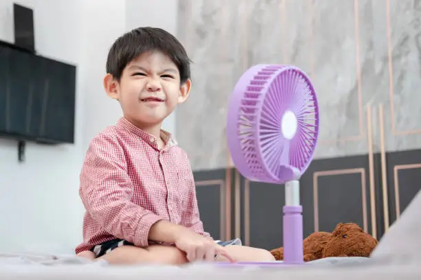 Photo of Asian boy Lying on the mattress on a hot day Playing with a portable fan happily