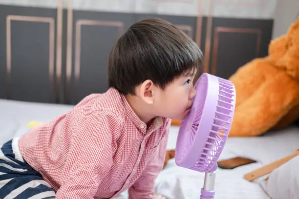 Photo of Asian boy Lying on the mattress on a hot day Playing with a portable fan happily