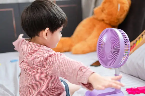 Photo of Asian boy Lying on the mattress on a hot day Playing with a portable fan happily