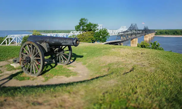 Close up of canon sitting on hill by Mississippi river auto and train bridges with miniature tilt-shift effect.  Horizontal panorama.