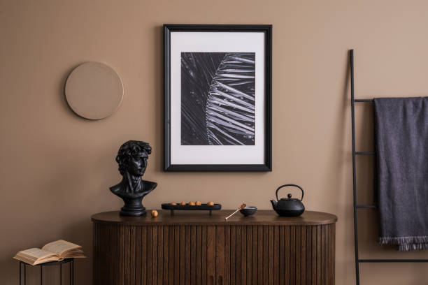 istock Creative composition of living room interior with mock up poster frame, wooden sideboard,  stylish sculpture, black ladder, plaid, beige wall, books and personal accessories. Home decor. Template. 1753850759