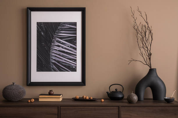 istock Creative composition of living room interior with mock up poster frame, wooden sideboard,  stylish sculpture, vase with branch, beige wall, books and personal accessories. Home decor. Template. 1753851417