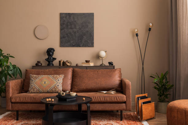 istock Stylish composition of living room interior with mock up poster frame, brown sofa, round coffee table, stylish lamp, round pouf, plants and personal accessories. Home decor. Template. 1753851421