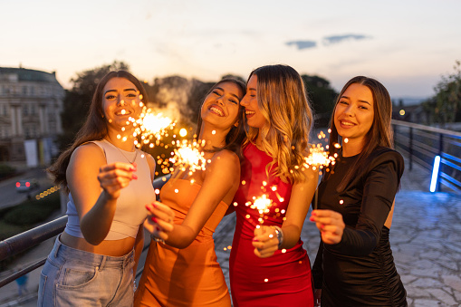 Group of young female friends having fun with sparklers in city together.