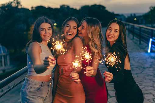 Group of young female friends having fun with sparklers in city together.