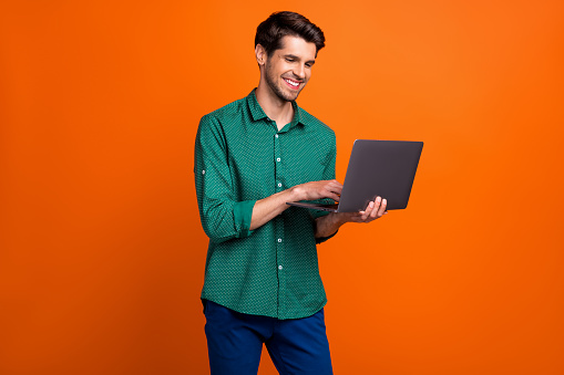Photo of cute cheerful man dressed green shirt texting apple samsung modern device isolated orange color background