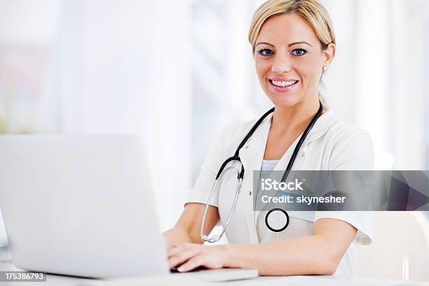 Foto de Sorrindo Feminino Médico Trabalhando Em Seu Laptop e mais fotos de stock de Adulto