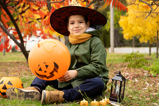 Happy Halloween kid playing with pumpkin balloon in park in autumn