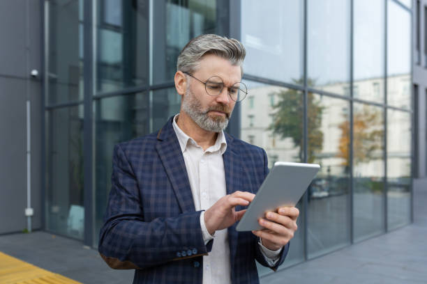 istock Serious thinking mature businessman outside office building using tablet computer, boss in business suit reading financial news on stock market, business owner walking in urban city 1753870868