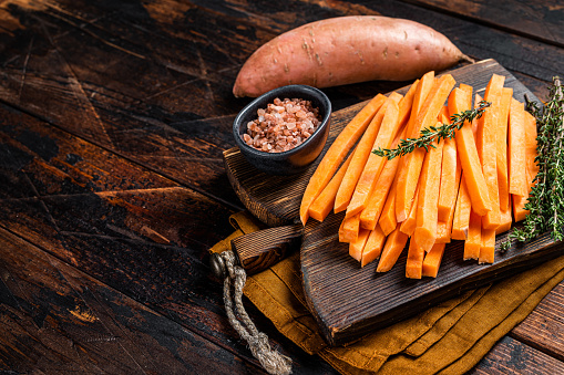 Sweet potatoes on a cutting board, fresh batata french fries ready for cooking. Wooden background. Top view. Copy space.