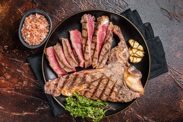 istock Grilled Medium rare Porterhouse, T-Bone Steak sliced in a plate. Dark background. Top view 1753873411