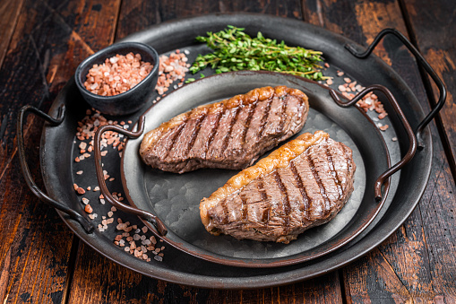 BBQ Grilled top sirloin steak, cup rump beef meat steak in a steel tray. Wooden background. Top view.