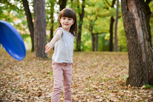 A little child girl is playing with a frisbee in the park during autumn day