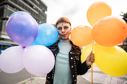 Portrait of a young non binary person holding balloons outdoors
