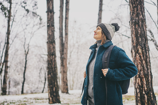 A young mature woman breathes fresh air and enjoys the snowfall in the winter forest. Winter walks and activity concept