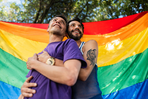 Gay couple embracing with rainbow flag on background