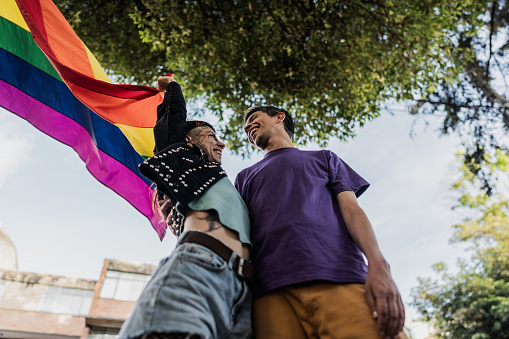 Lgbtqia+ friends embracing holding rainbow flag outdoors