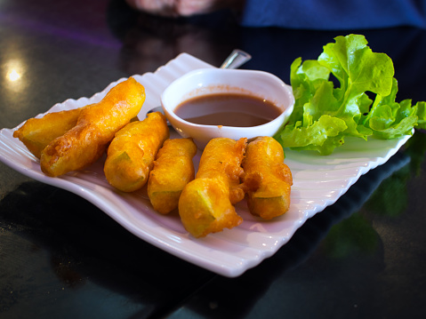 A plate of Burmese golden crispy fritters entree made from gourd commonly known in Myanmar as 'buthee gyaw', served with a tamarind-based sauce and green lettuce.