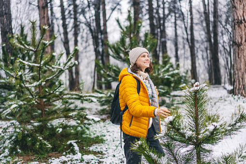 Young  adult caucasian woman in a hat and yellow jacket breathing fresh air in the winter forest