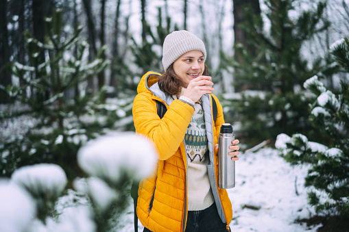 Young woman with a thermos in a snowy forest. Winter walks and activity concept