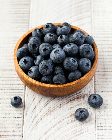 Juicy ripe blueberries in a wooden plate on a white wooden background. The concept of berries.