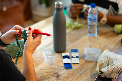 Crochet club. Young woman with red painted nails knitting.