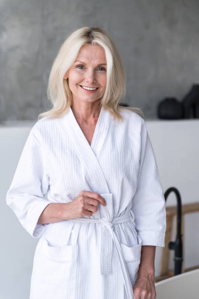 istock Senior woman in bathrobe standing in bathroom, look at camera 1753896125
