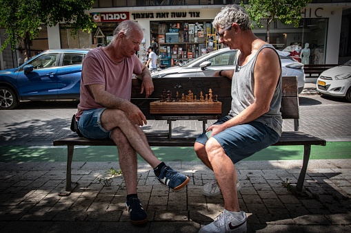 Jerusalem, Israel – August 09, 2023: Two adult Caucasian men wearing casual clothing sitting on a wooden bench in a relaxed manner, enjoying the outdoor setting