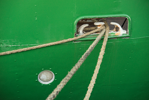 Roped going through a mooring hole of a green metal ship.