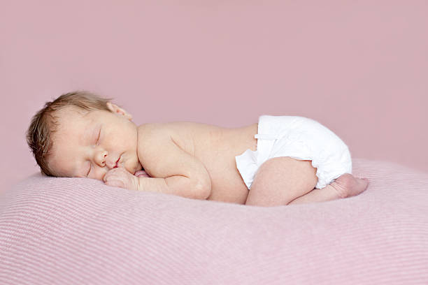 Full length newborn baby girl asleep on tummy. Pink background. stock photo