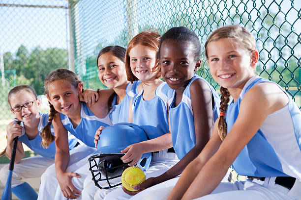niñas de softball equipo de estar en el banquillo de campo de béisbol - campeonato deportivo juvenil fotografías e imágenes de stock
