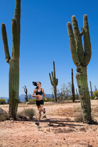 A female athlete at peak action, running amongst old Saguaros in the desert.