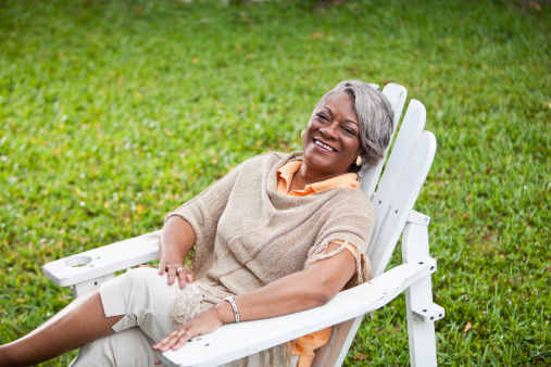 Stylish mature African American woman (50s) sitting in adirondack chair.