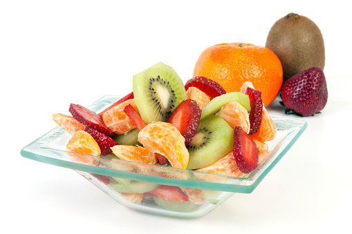 Portion of strawberries, tangerines and kiwi in glass bowl prepared for eating. Isolated on white background.
