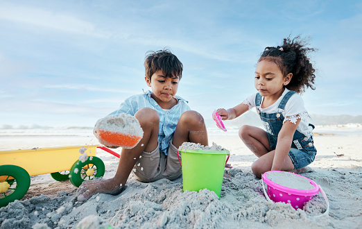 Boy, girl and shovel with bucket, beach sand and digging for  playing, outdoor and vacation in summer. Kids, siblings and plastic toys for sandcastle, construction game and together on holiday by sea